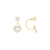 A pair of yellow gold hoop earrings with clear gemstones, shown on a clean light gray gradient background. One earring is shown front-facing, featuring a small round stone above a flower-like cluster of heart-shaped stones.