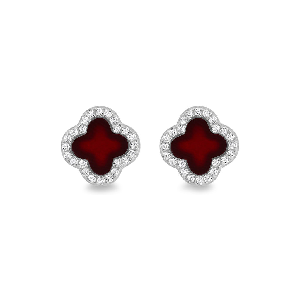A pair of clover-shaped stud earrings featuring deep red enamel centers surrounded by a border of small clear stones in a silver-tone setting, shown on a plain white background